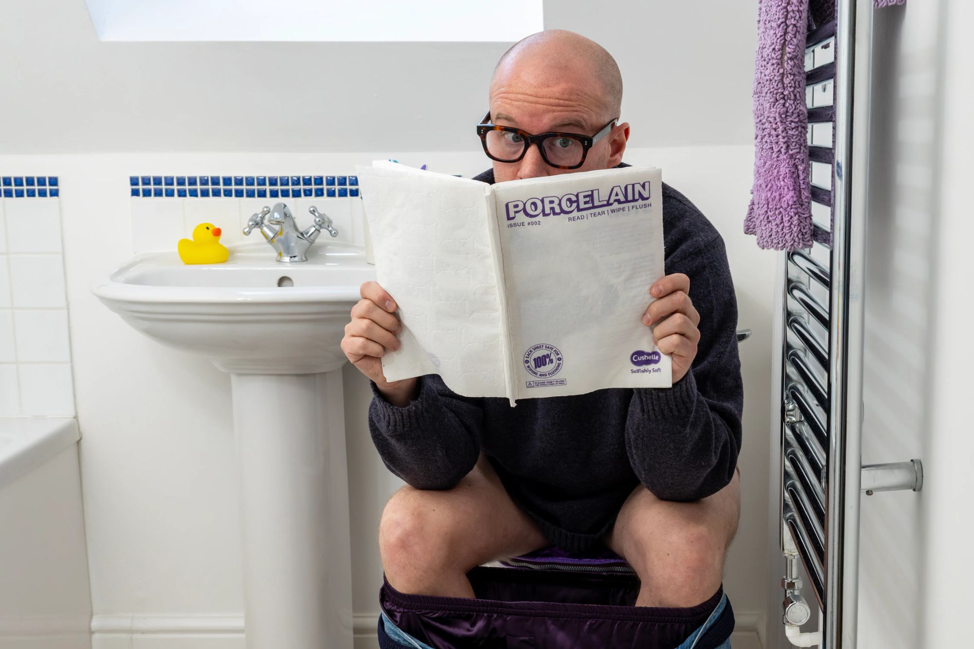An image collage containing 1 images, Image 1 shows A man in glasses sitting on a toilet with his jeans around his ankles, holding up a magazine titled "Porcelain" that reads "Read | Tear | Wipe | Flush"