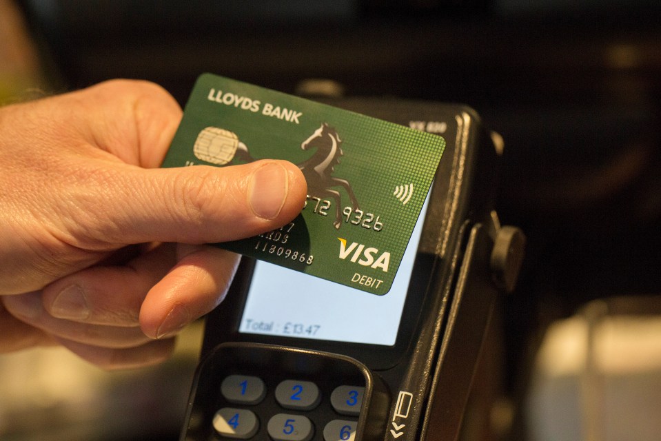 A hand using a Lloyds Bank Visa debit card for a contactless payment.