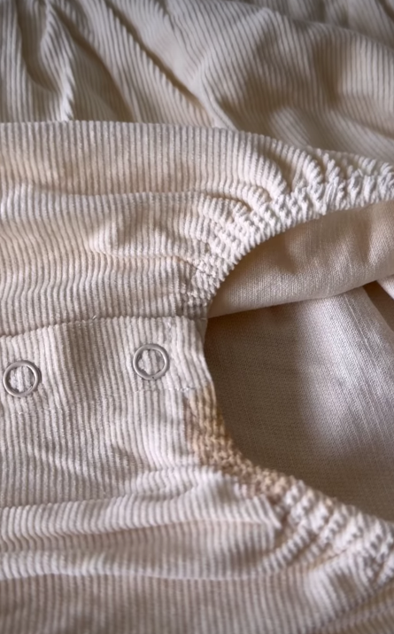 Close-up of a baby's cream-colored corduroy romper with two snaps at the crotch and a stain near the leg opening.