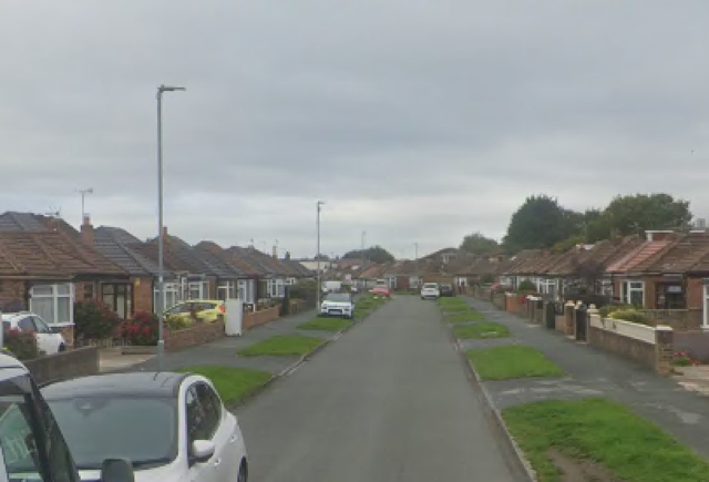Street view of a residential neighborhood with bungalows lining both sides of the road under a cloudy sky.