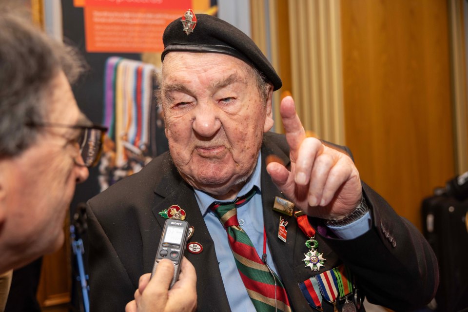 Richard Aldred, a 99-year-old D-Day veteran, is interviewed while wearing a beret, medals, and a striped tie.