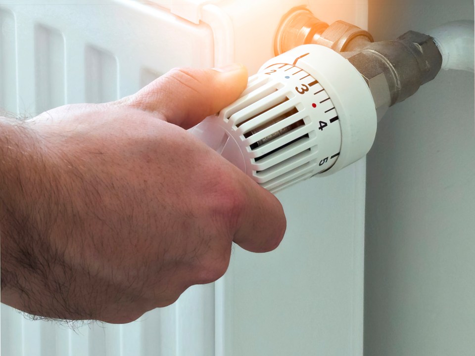 A hand adjusting the thermostat on a white radiator.