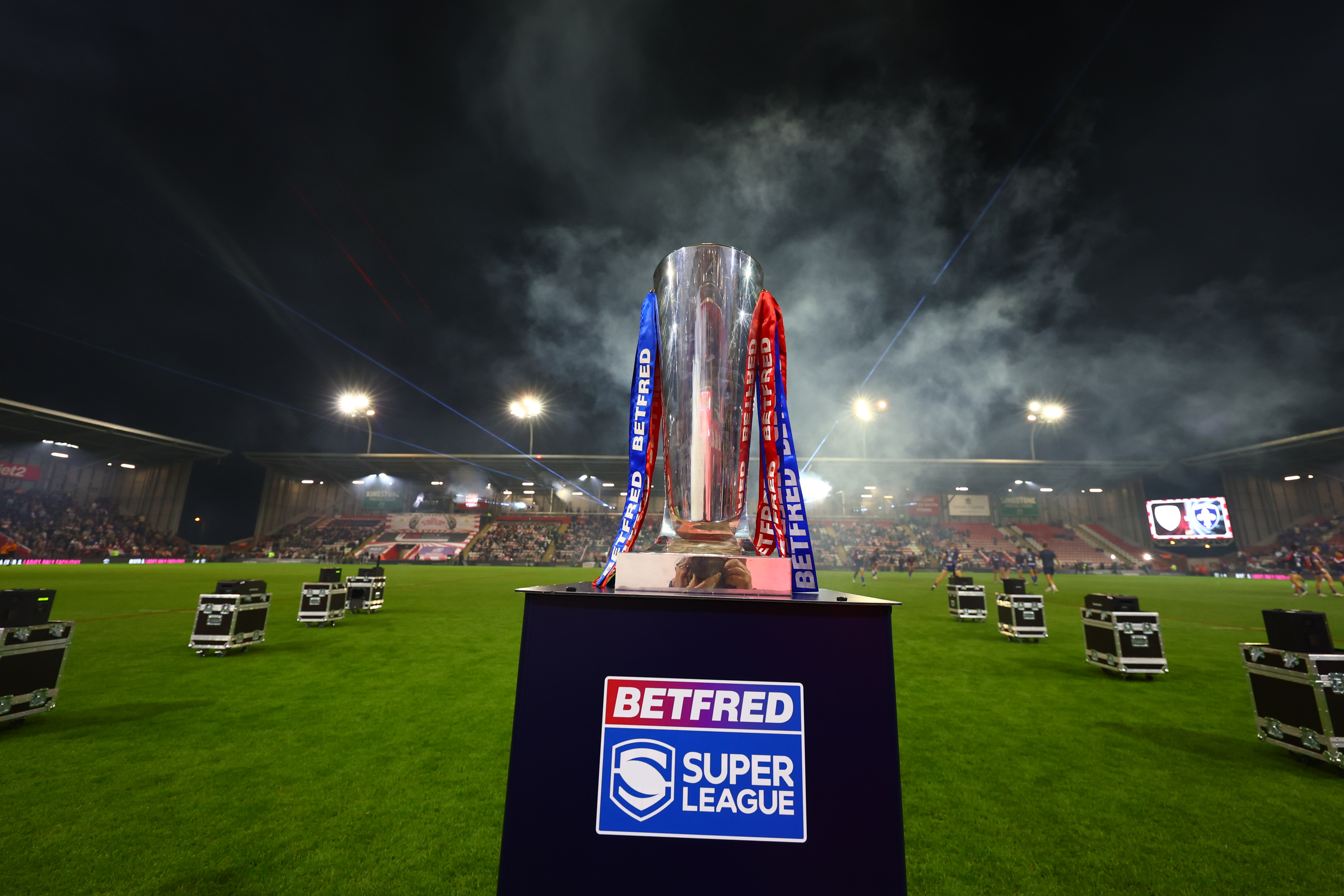 Betfred Super League trophy on a podium at a stadium field at night.