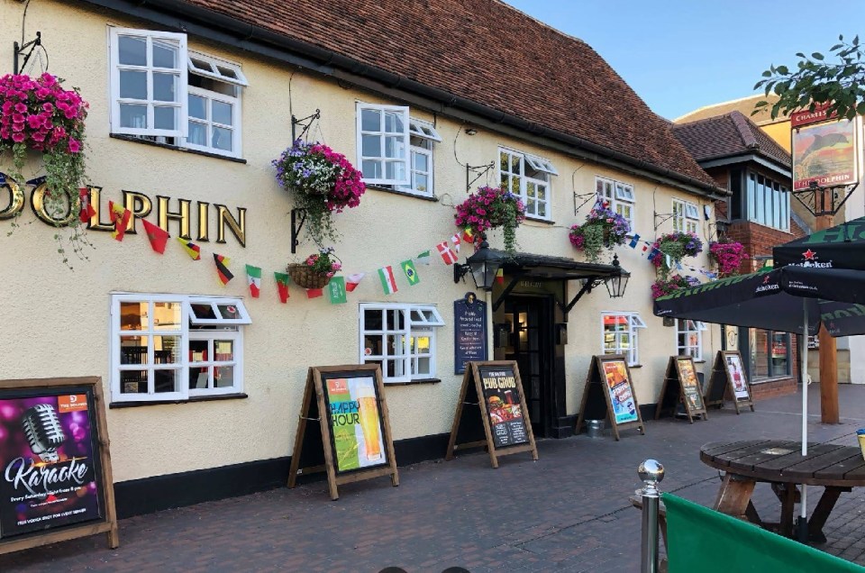 The Dolphin pub in Newport Pagnell, located at 82 High St, Newport Pagnell MK16 8AQ, with multiple signs advertising karaoke and happy hour.
