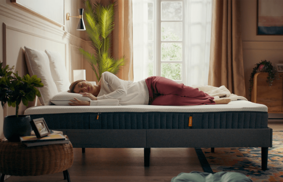 A woman sleeping on her side on a mattress with an Emma logo.