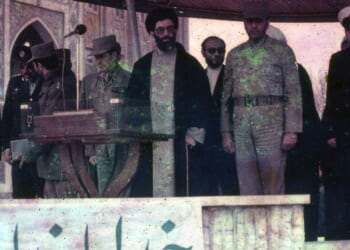 Iranian President Ali Khamenei surrounded by soldiers on stage in March of 1983.