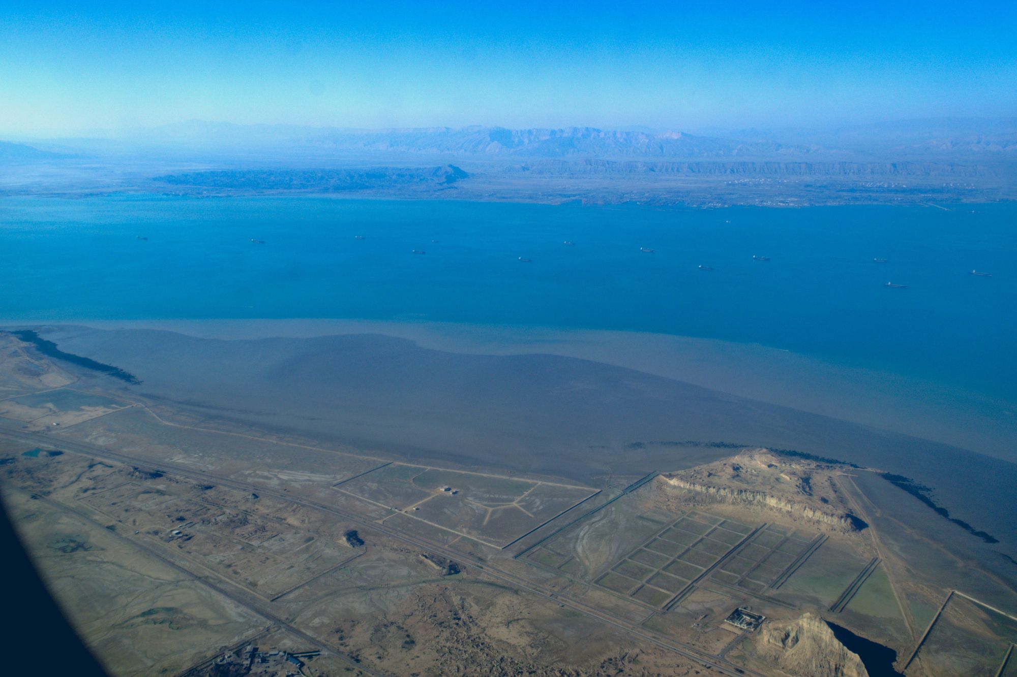 An image collage containing 1 images, Image 1 shows Aerial view of Khoran Strait, Qeshm Island, and the Iranian mainland with cargo and oil ships in the Strait of Hormuz