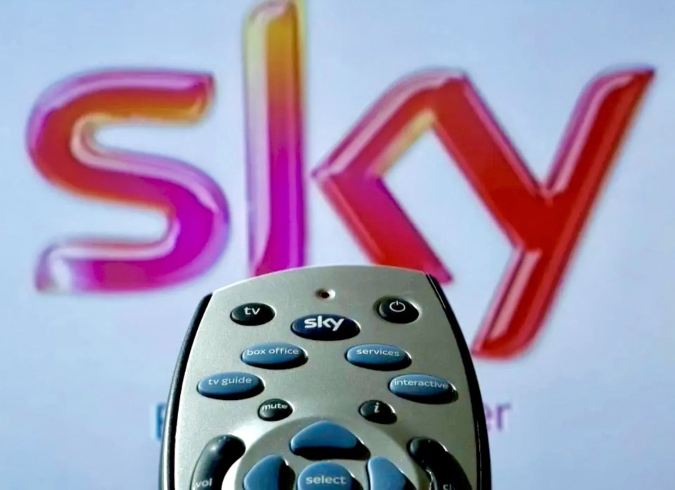 A Sky TV remote control in the foreground with the Sky logo blurred in the background.