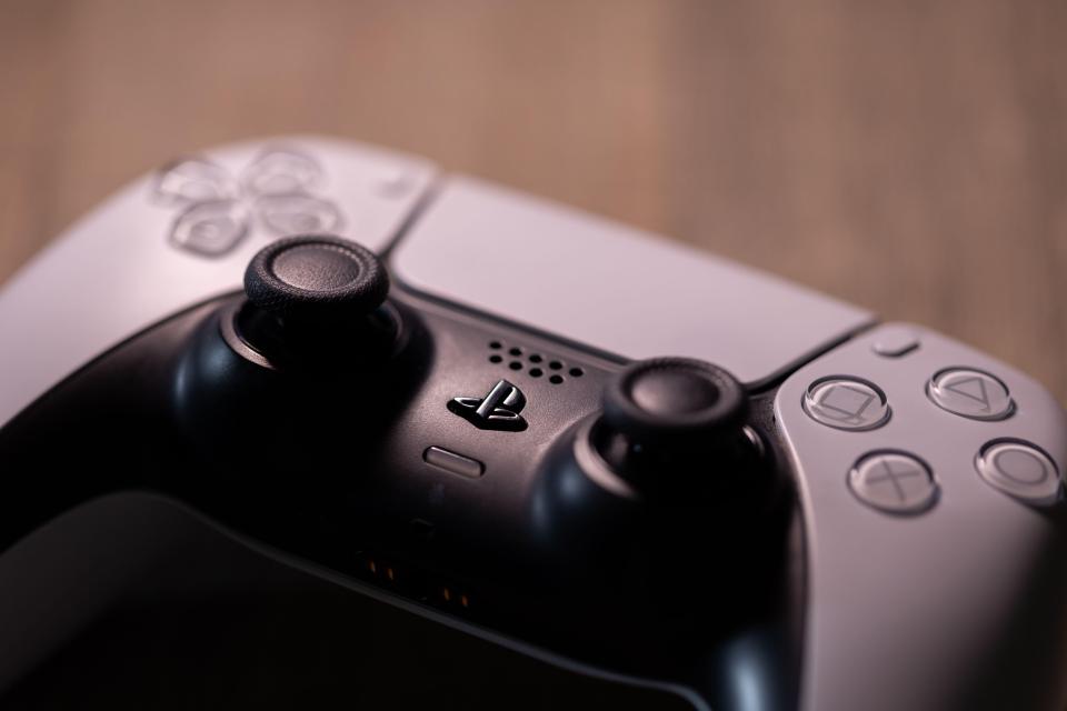 A close-up of a white Sony PlayStation 5 wireless controller on a wooden table.