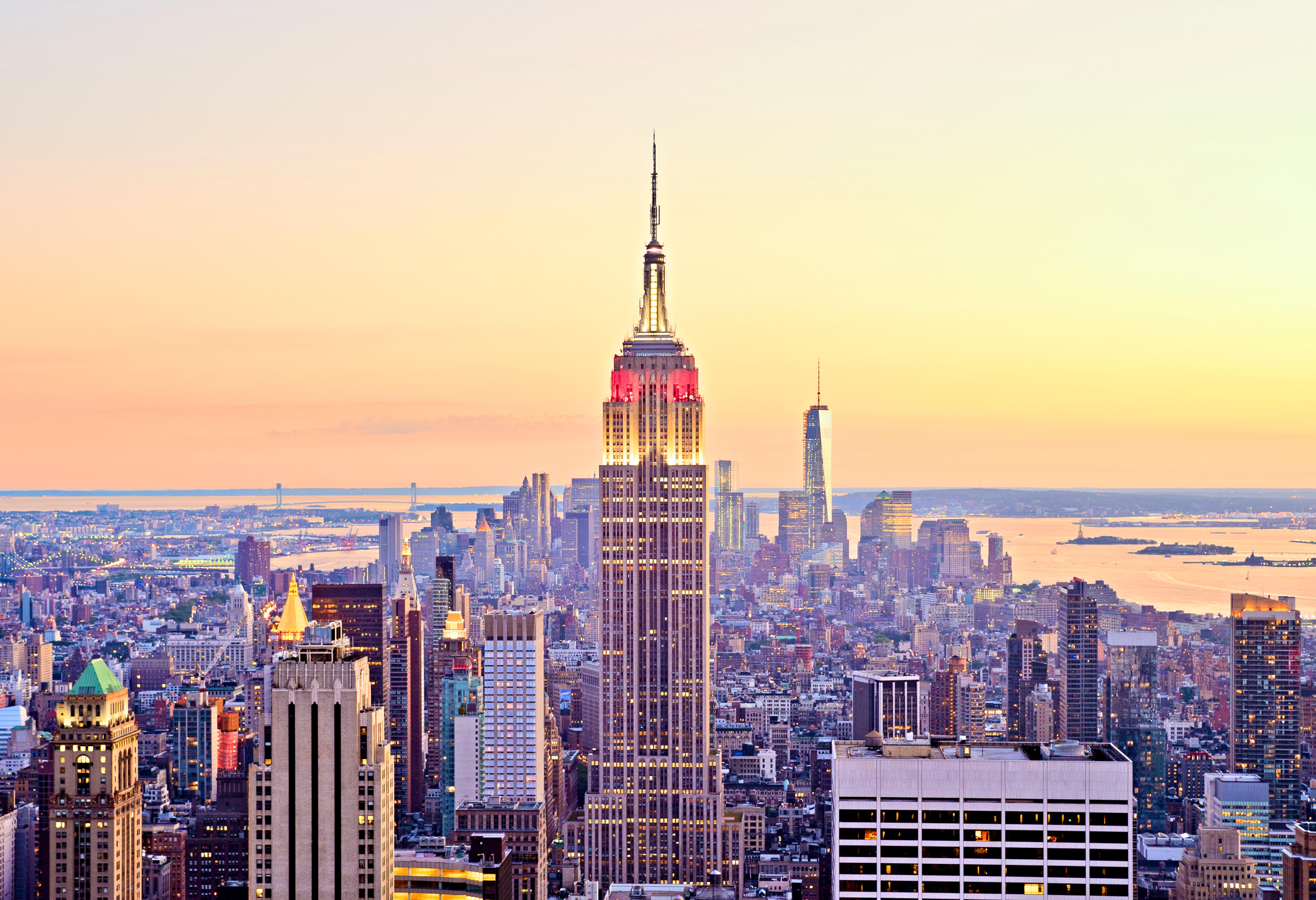 Aerial view of the New York City skyline with the Empire State Building prominent in the center, lit in red and white against a sunset sky.