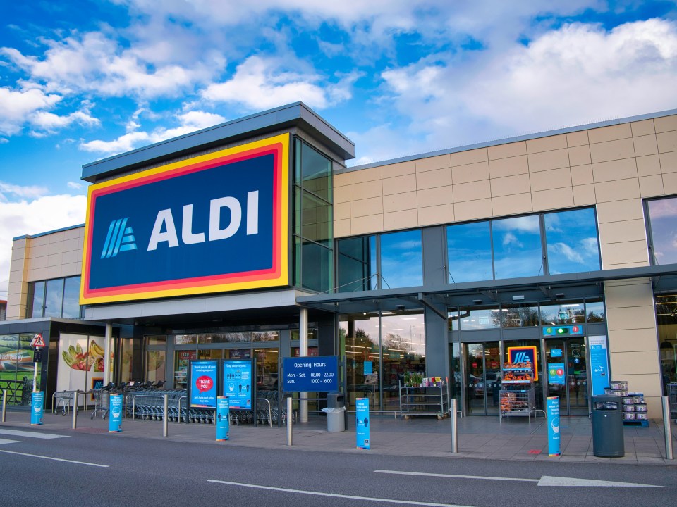 Exterior of an Aldi supermarket with its large blue and white logo, featuring colorful stripes, under a clear blue sky.