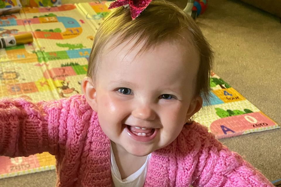An image collage containing 1 images, Image 1 shows A smiling baby in a pink cardigan leans over a couch, holding a black remote