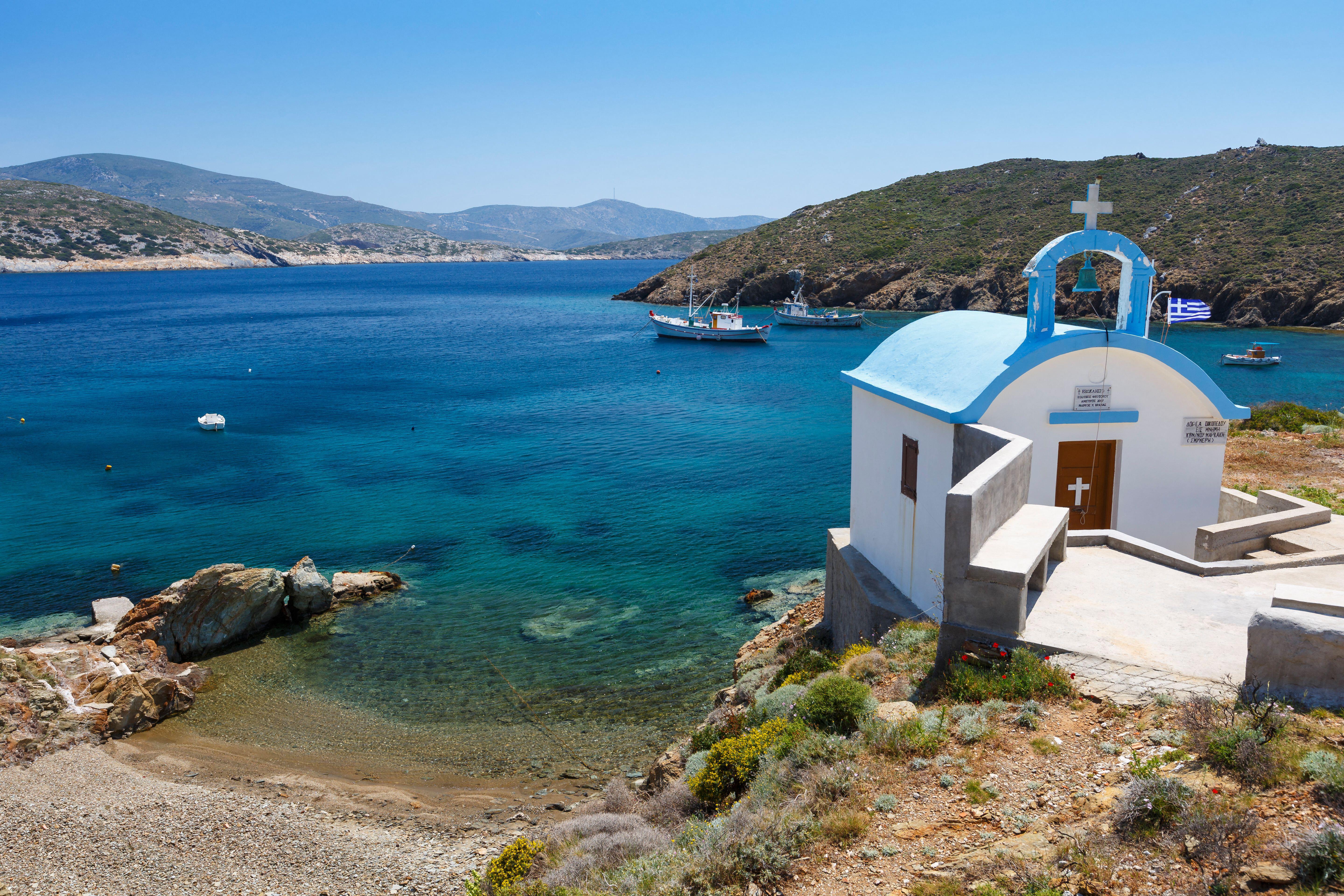 Keramidou beach on Thymaina island with a chapel, two fishing boats, and other smaller boats.
