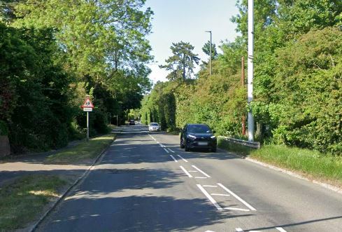 Road A355 in Buckinghamshire with green trees and hedges lining both sides, and a black car driving in the foreground.