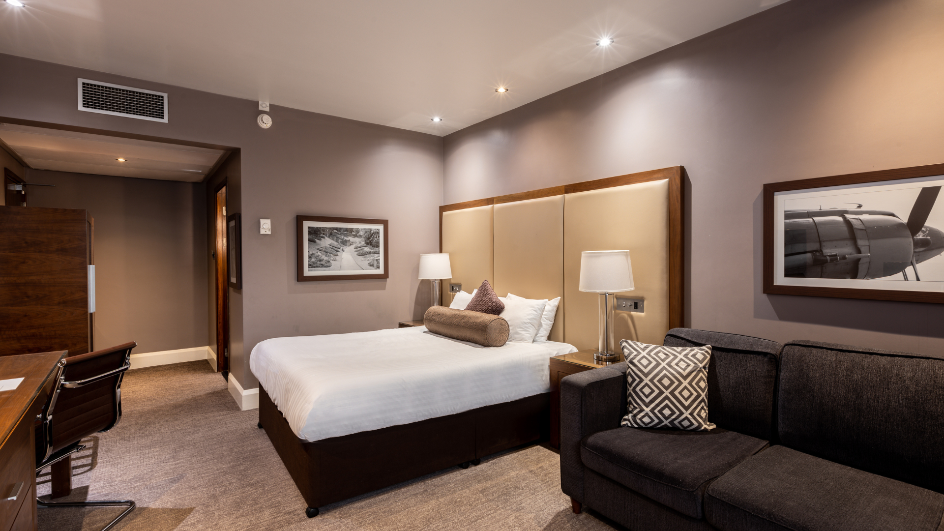 A hotel room at the Sandman Signature London Gatwick Hotel with a bed, desk, and sofa.