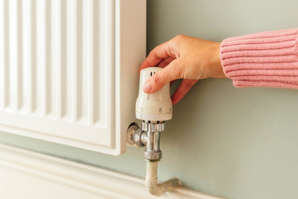 A woman's hand adjusts the thermostat dial on a white radiator.