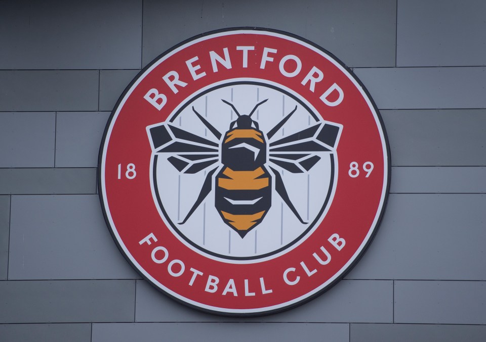 Close-up of the Brentford Football Club logo, featuring a bee in the center, on a grey wall.