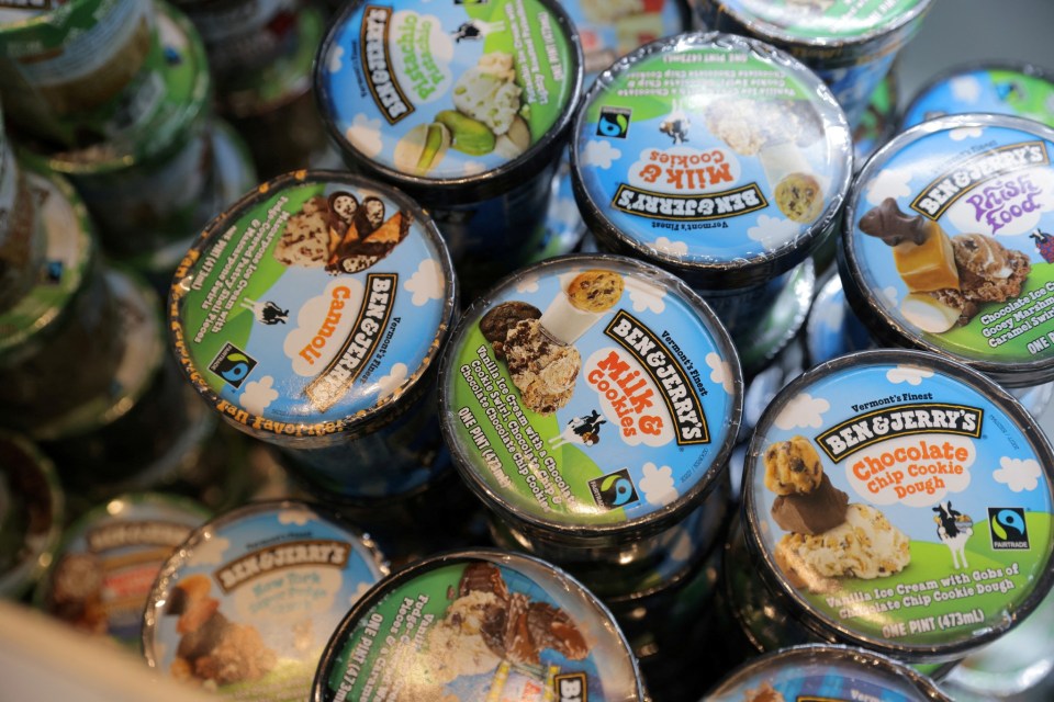 Several Ben & Jerry's ice cream pints in a store display, featuring various flavors like Chocolate Chip Cookie Dough, Cannoli, Milk & Cookies, and Pistachio.