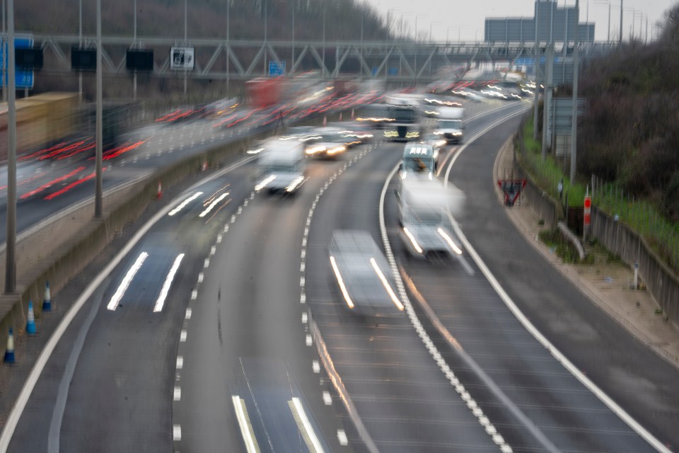 Blurred image of the M25 motorway with heavy traffic, showcasing light trails from vehicle headlights and taillights.