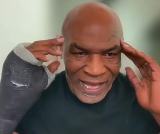 Mike Tyson wearing an arm cast, touching his head with both hands.