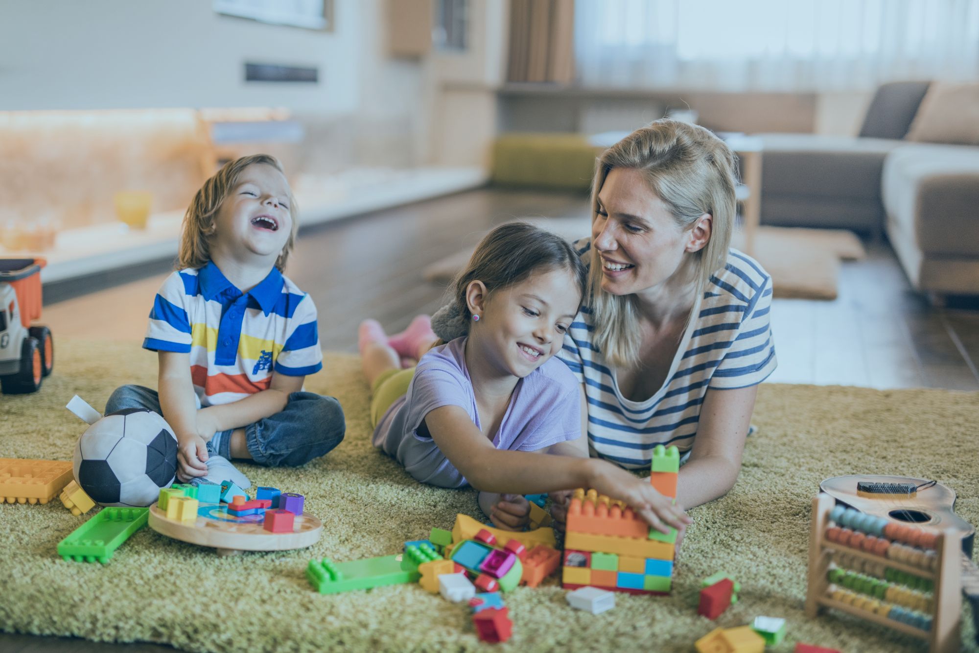 An image collage containing 1 images, Image 1 shows Mother and children playing with toys on a carpet in the living room