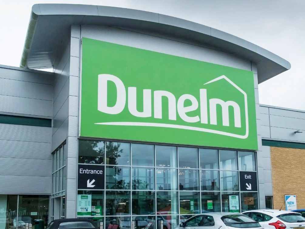 The front exterior of a Dunelm store, featuring its green logo above glass windows, and entrance/exit signs.