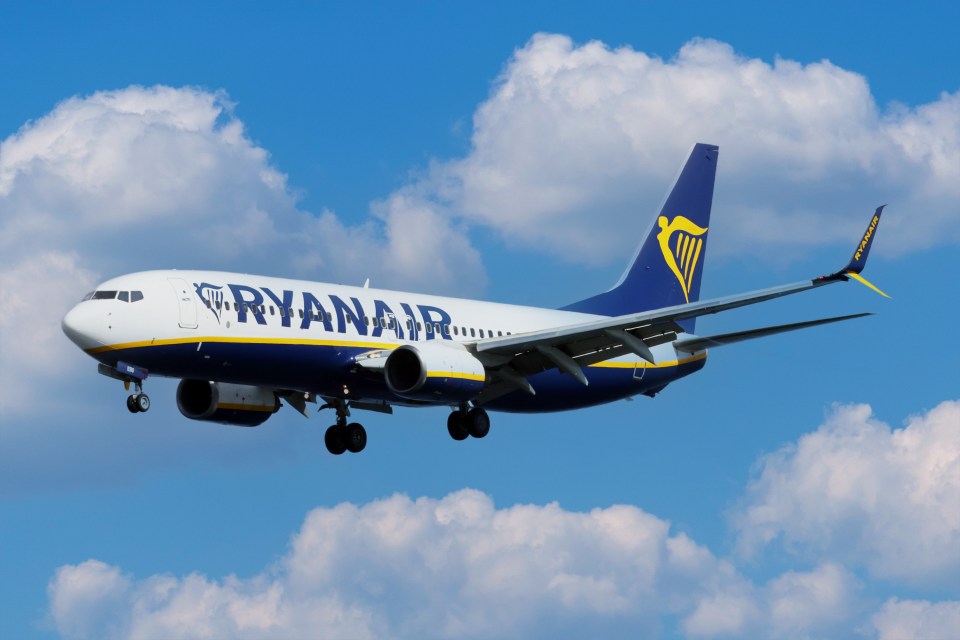 A Ryanair airplane in flight against a cloudy blue sky.