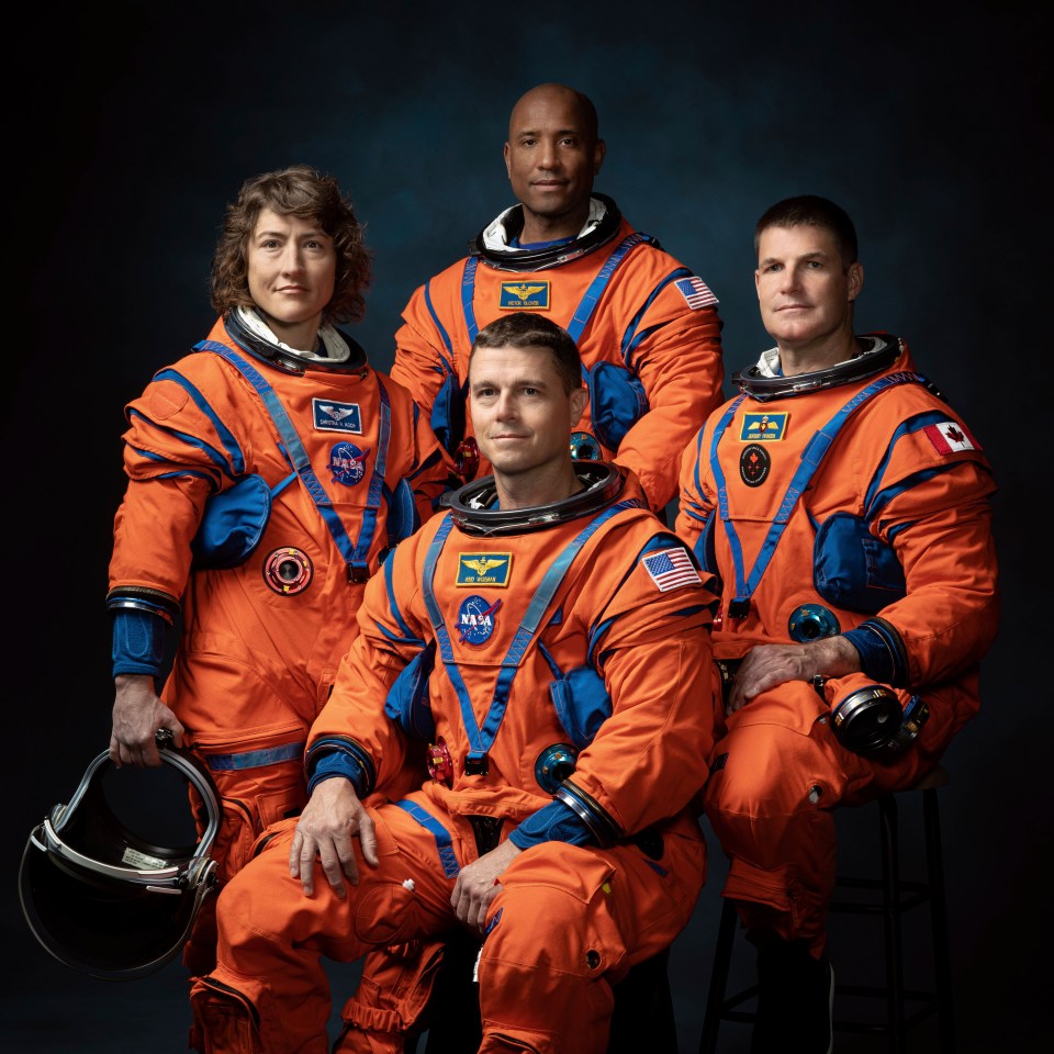 Four astronauts in orange suits pose against a dark background.