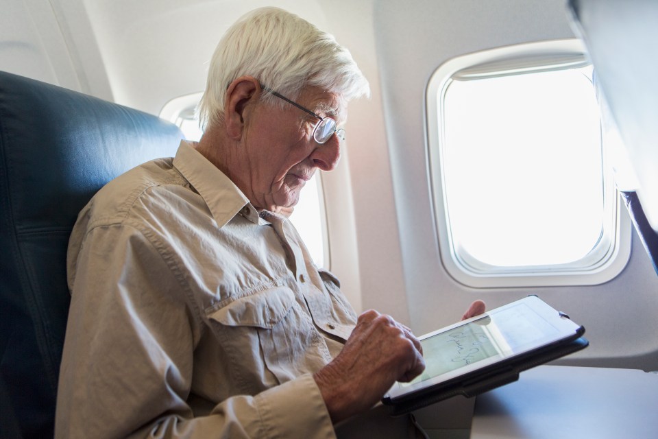 Elderly man using a tablet computer on an airplane.