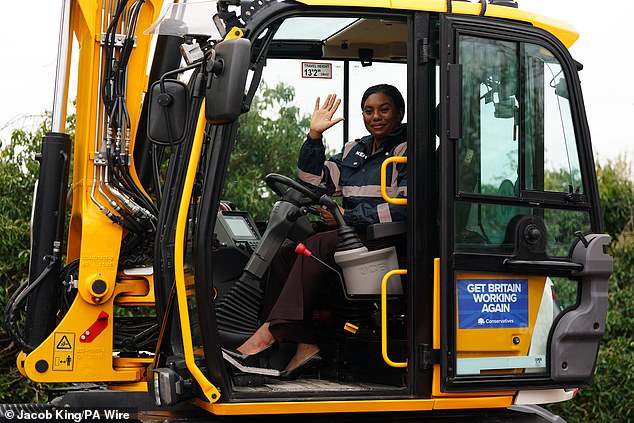 Kemi Badenoch waves from the driving seat of a construction vehicle during a visit to Knowle football club in the West Midlands