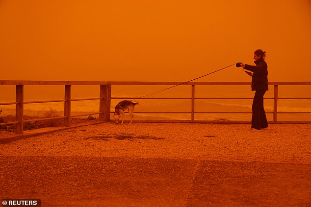 A woman walks her dog amid the haze on the Greek Island, a popular tourist destination
