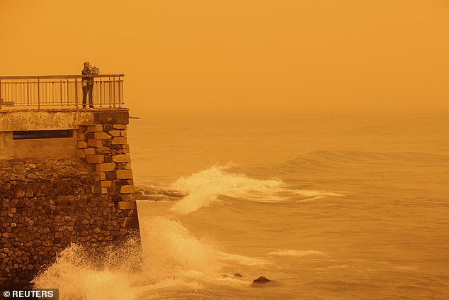 A woman takes pictures of the horizon turned yellow, caused by sand dust from the Sahara, due to strong southern winds, in Heraklion, Crete island, Greece April 1