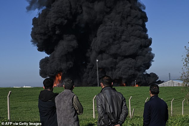 People watch as smoke billows from an oil warehouse in the Kani Qirzhala area on the outskirts of Erbil, the capital of Iraq's autonomous Kurdistan region, following a suspected drone strike, on April 1, 2026. Iraq has been drawn into the broader Middle East war