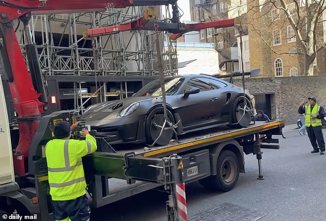 Two men in high-visibility jackets help guide it on to the truck before it is driven off to be impounded