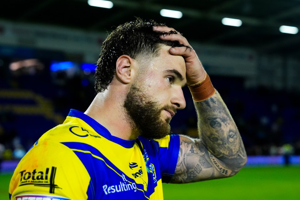 Connor Wrench, a rugby player with a beard and tattoos, wearing a yellow and blue jersey, with his hand on his head.