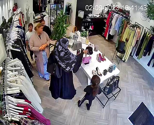 Security footage (pictured) captures her eyeing the 'pre-loved' £6,000 bag like a coveted toy, then alerting a woman wearing a flowery headscarf who is feigning interest in dresses