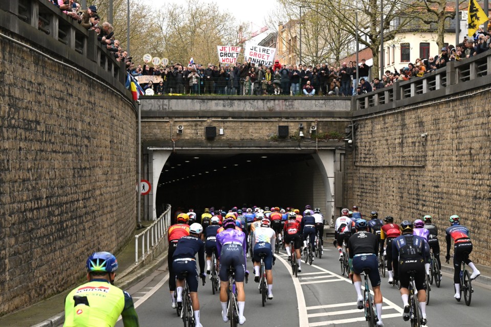 Cyclists entering a tunnel with spectators on the overpass.