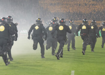 Shocking moment riot police chase football ultras off pitch while flares are hurled down in fiery clash