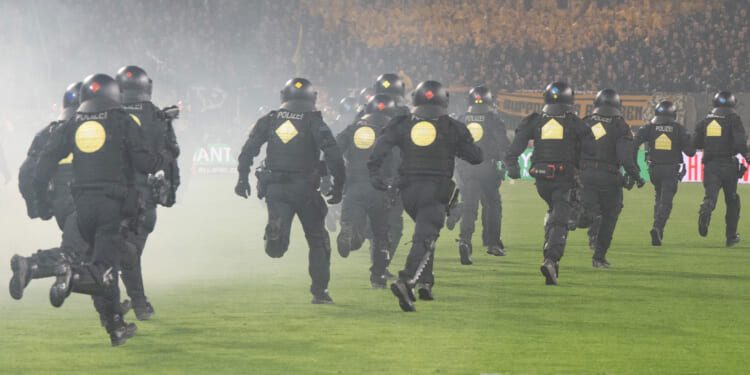 Shocking moment riot police chase football ultras off pitch while flares are hurled down in fiery clash