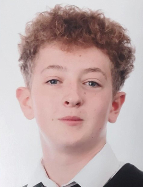 A 13-year-old boy with mousey brown/red curly hair, a slim build, and light-colored eyes.
