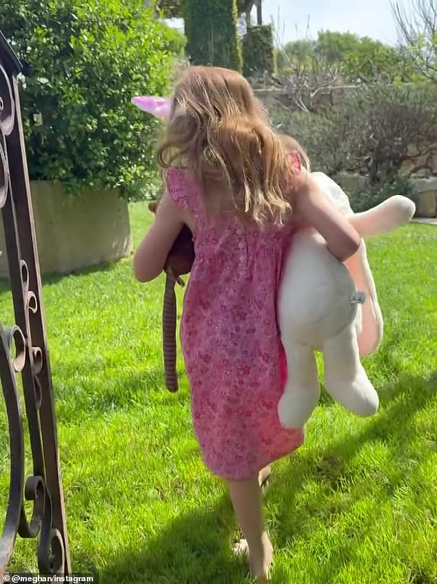 Lilibet clutches a large toy bunny as she wanders through a garden in the spring sunshine