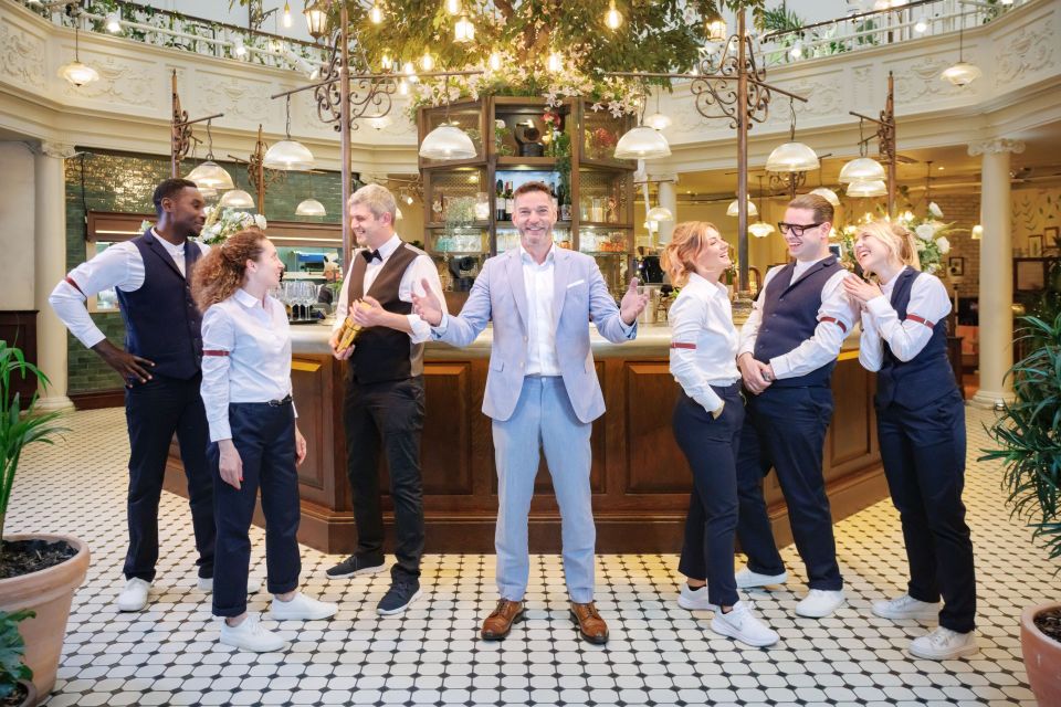 Six hospitality workers and a man in a light blue suit smile and laugh in a bar area.
