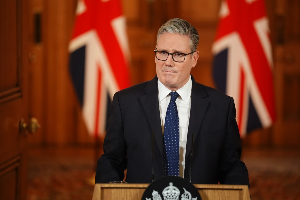 Prime Minister Sir Keir Starmer speaking at a podium with two Union Jack flags in the background.