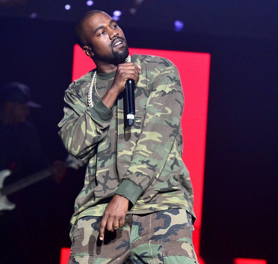 Kanye West performing in a camouflage outfit, holding a microphone.