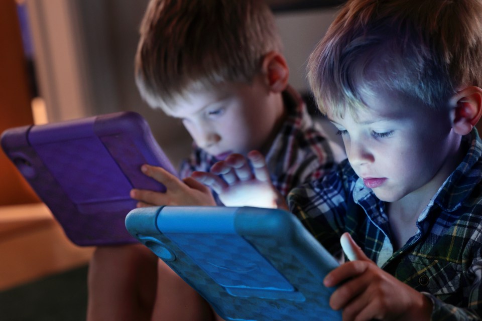 Two young boys looking intently at computer tablets in a dimly lit room.