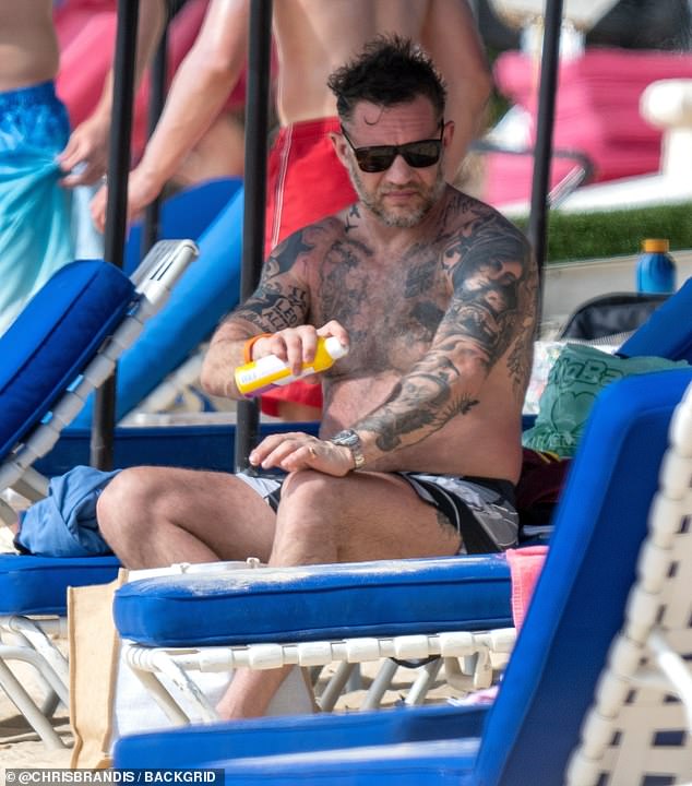Tom was seen smearing sun cream onto his body while perched on a sunbed