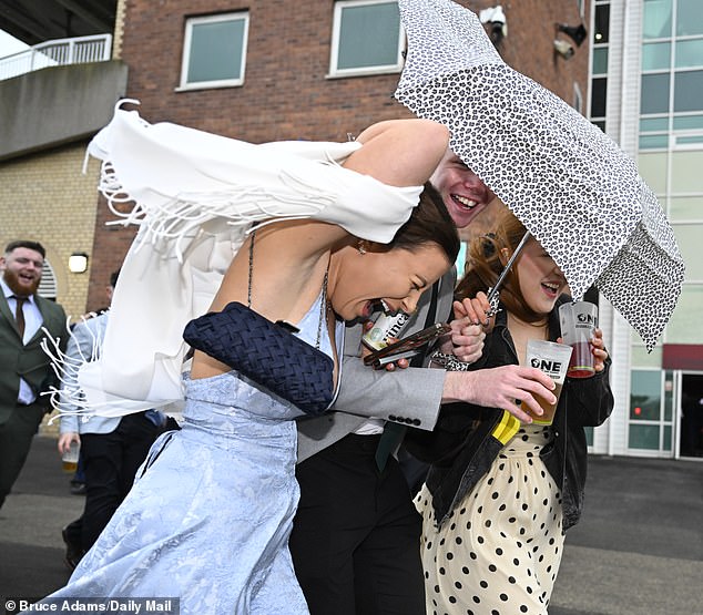 Take cover! Revellers struggle against the wind and the rain as they walk around the racecourse