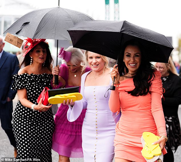 No raining on their parade! Beaming racegoers shelter from the rain on day one of the Randox Grand National Festival 2026