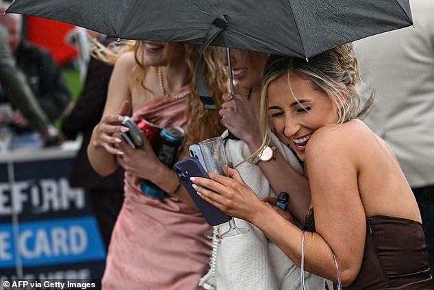 Racegoers shelter under an umbrella as they arrive in cool, wet weather to attend the opening day of the Grand National Festival