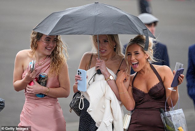 Female racegoers in strappy dresses huddled together under a brolly to stay dry
